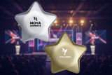 Two star-shaped stress balls, one silver with Moya Airways logo and one gold with Colibri logo, on a white background.